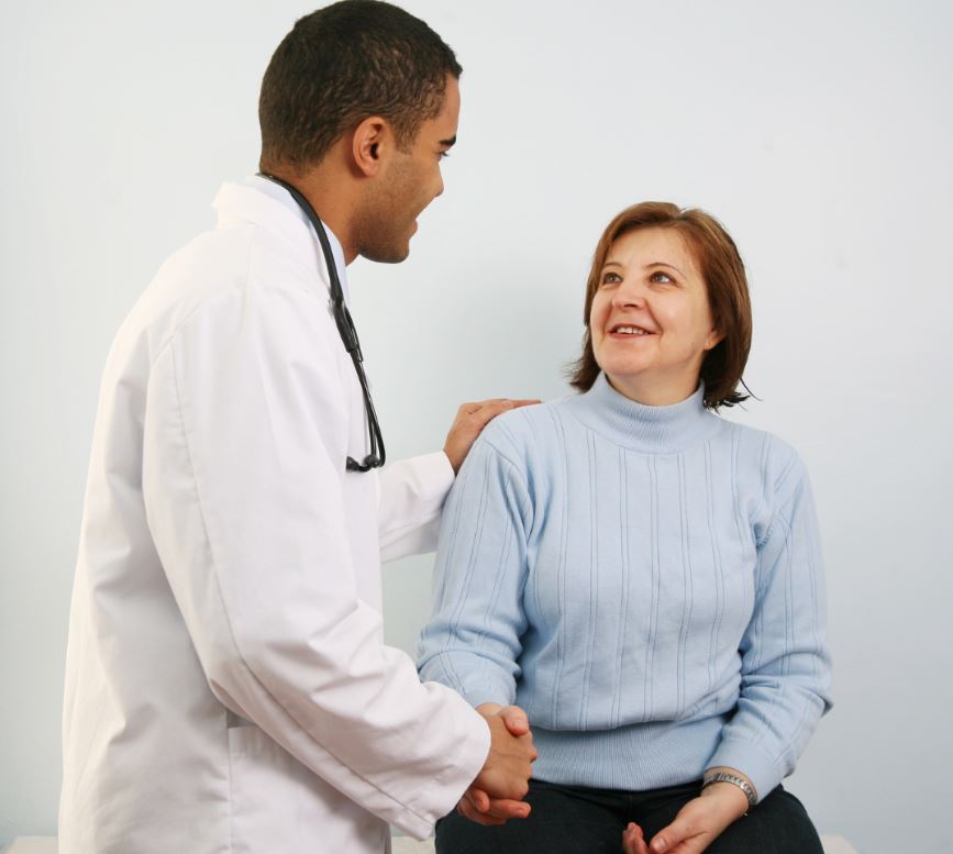 A medical professional shakes hands with a patient seated on a examination table.