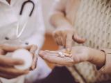 An older woman with a handful of oral medications.
